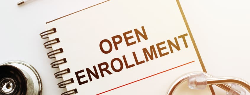 Notebook with open enrollment written on the cover with a stethoscope and a thermometer next to it.