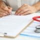 Close-up of female doctor in medical gown put sign on clipboard with documents. Qualified worker made prescription for patient. Medicine, clinic concept